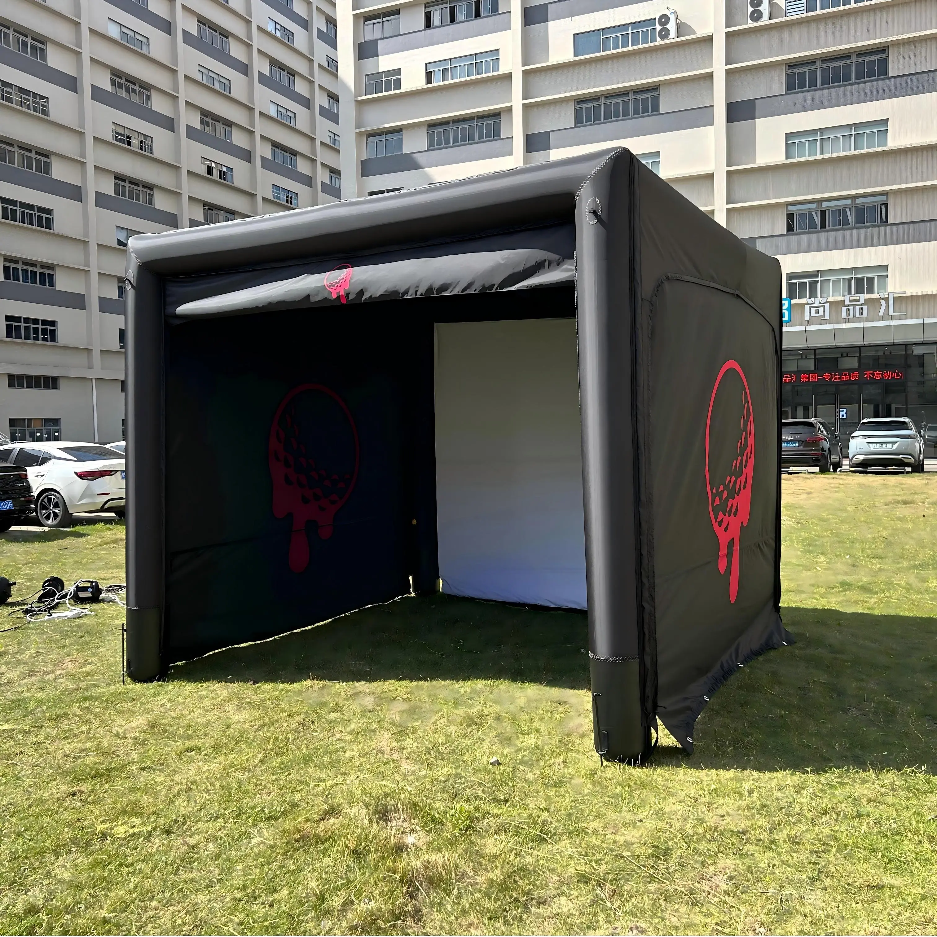 Black air-sealed inflatable golf simulator enclosure set up on outdoor grass with red golf ball graphic.